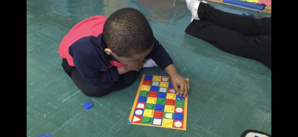 child matching plastic colorful shapes with corresponding spaces on a mat on the floor