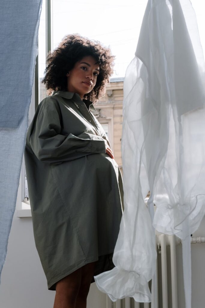 pregnant woman in gray long sleeves holding her baby bump while smiling at the camera